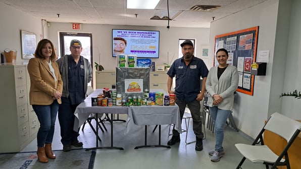 Four individuals standing near a table filled with various products.